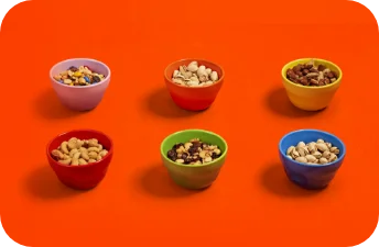 Cashews, pistaccios, and mixed nuts are displayed in colorful bowls against an orange surface.