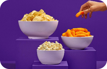 Potato chips, cheese puffs, and popcorn are displayed in bowls on a tiered purple display.